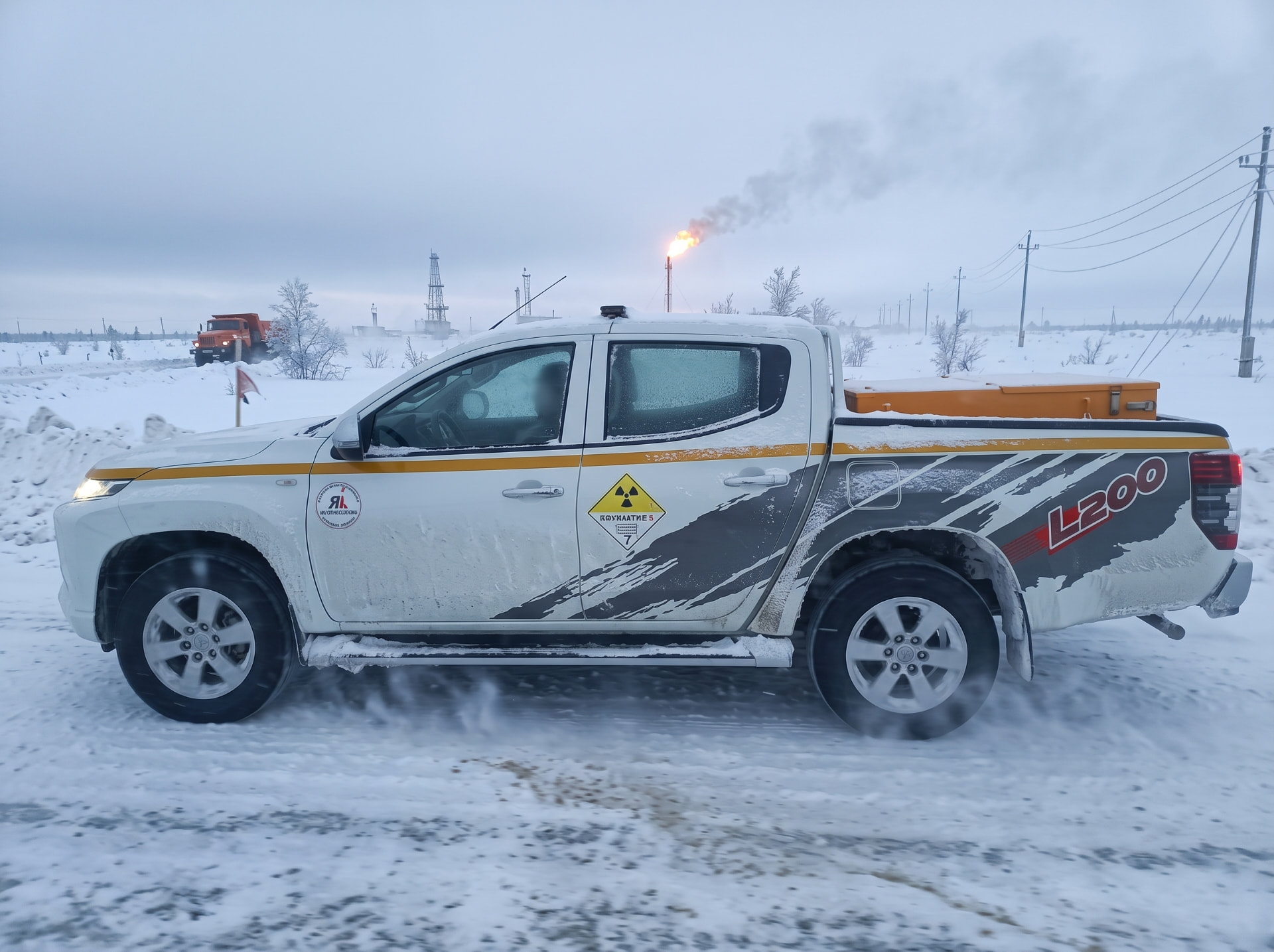Mitsubishi L200 компании со знаком опасности класса 7 на промысле, вид сбоку
